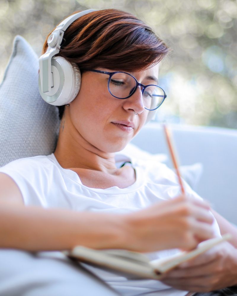 Young woman, inlingua Andorra student, with glasses and headphones writing on a piece of paper